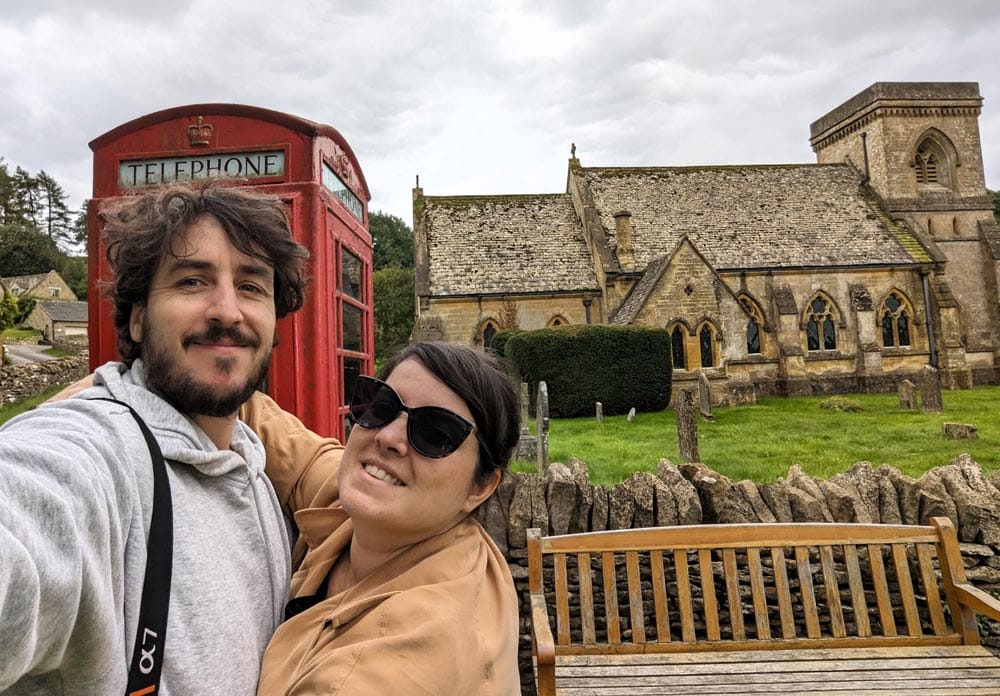 viajeros en los Cotswolds con cabina roja y antigua iglesia al fondo